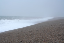 Looking west along Chesil beach from the Isle of Portland on a sunny day  with an onshore wind that has created some surf. Some anglers can be seen  fis Stock Photo 